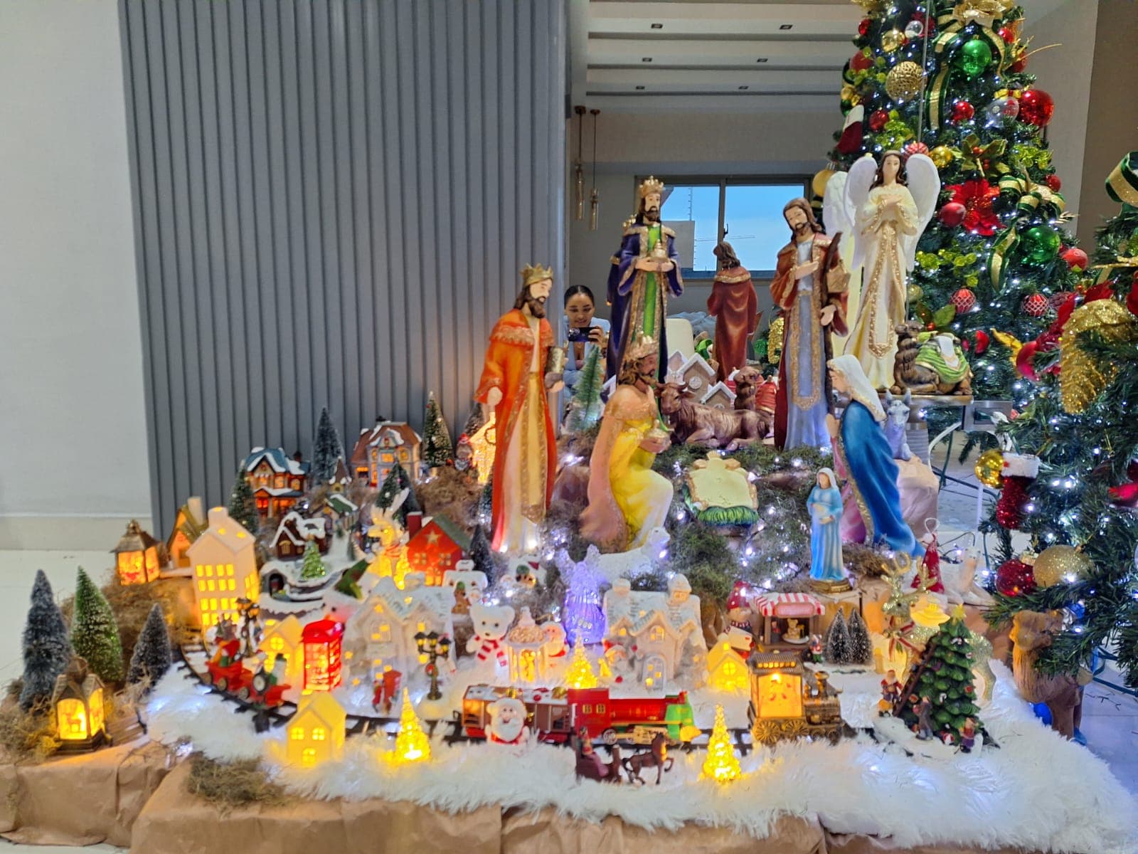 Árbol de Navidad con nacimiento y villa en miniatura al pie, en una sala.