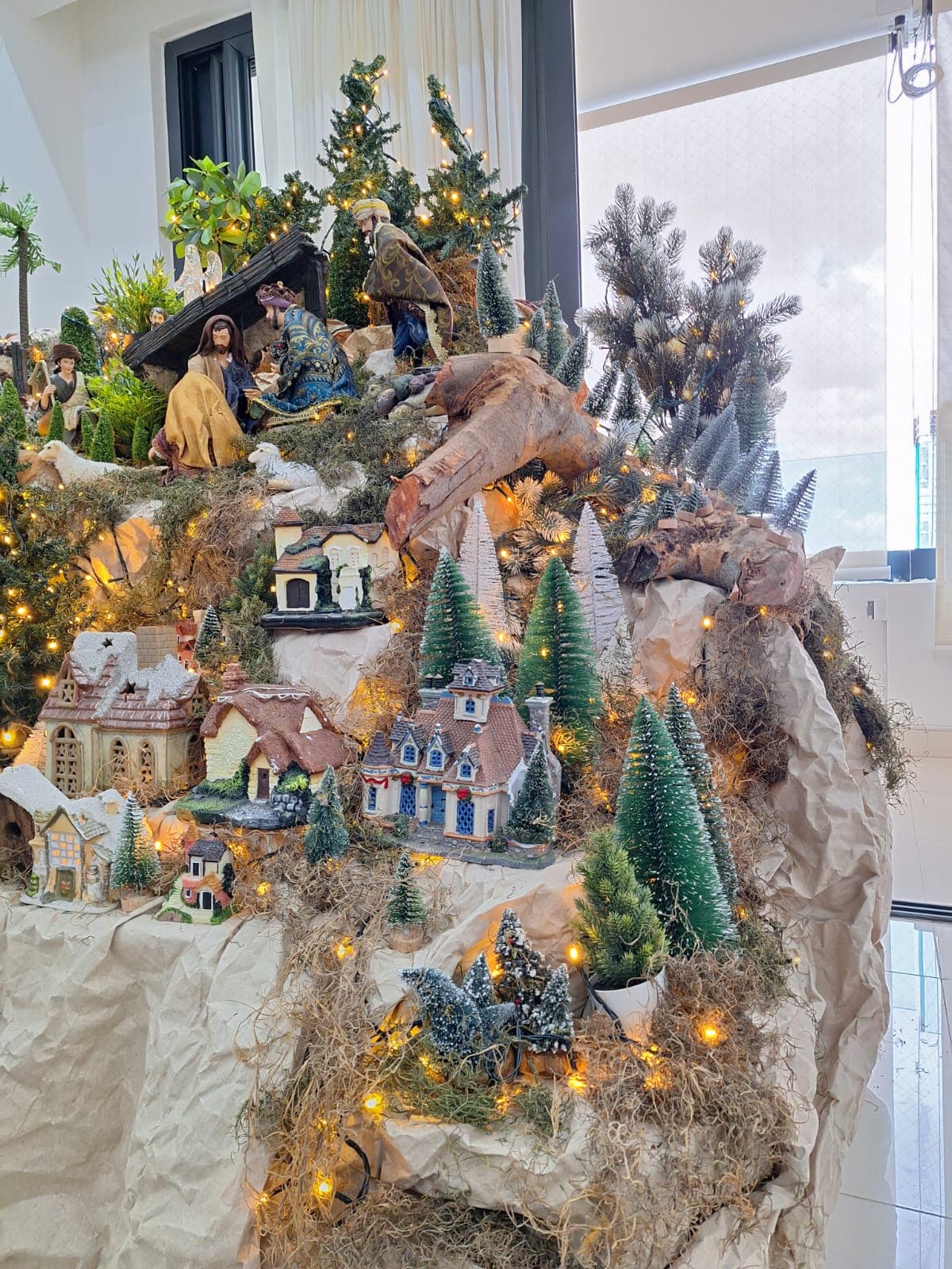 Villa navideña con casas iluminadas entre musgo y pinos nevados.